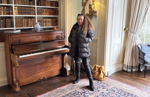 Author, lady standing next to a piano in a library. titled About.