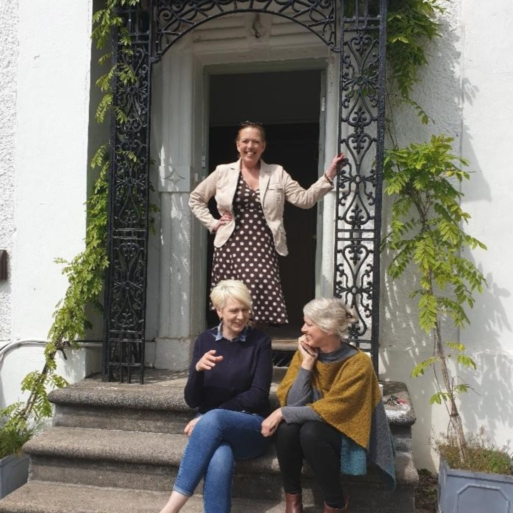 Women at front door and two women sitting on the steps chatting.